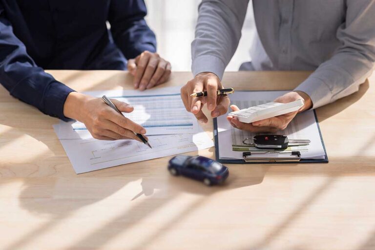 A woman discusses an insurance claim with her agent while looking at paperwork at her kitchen table.